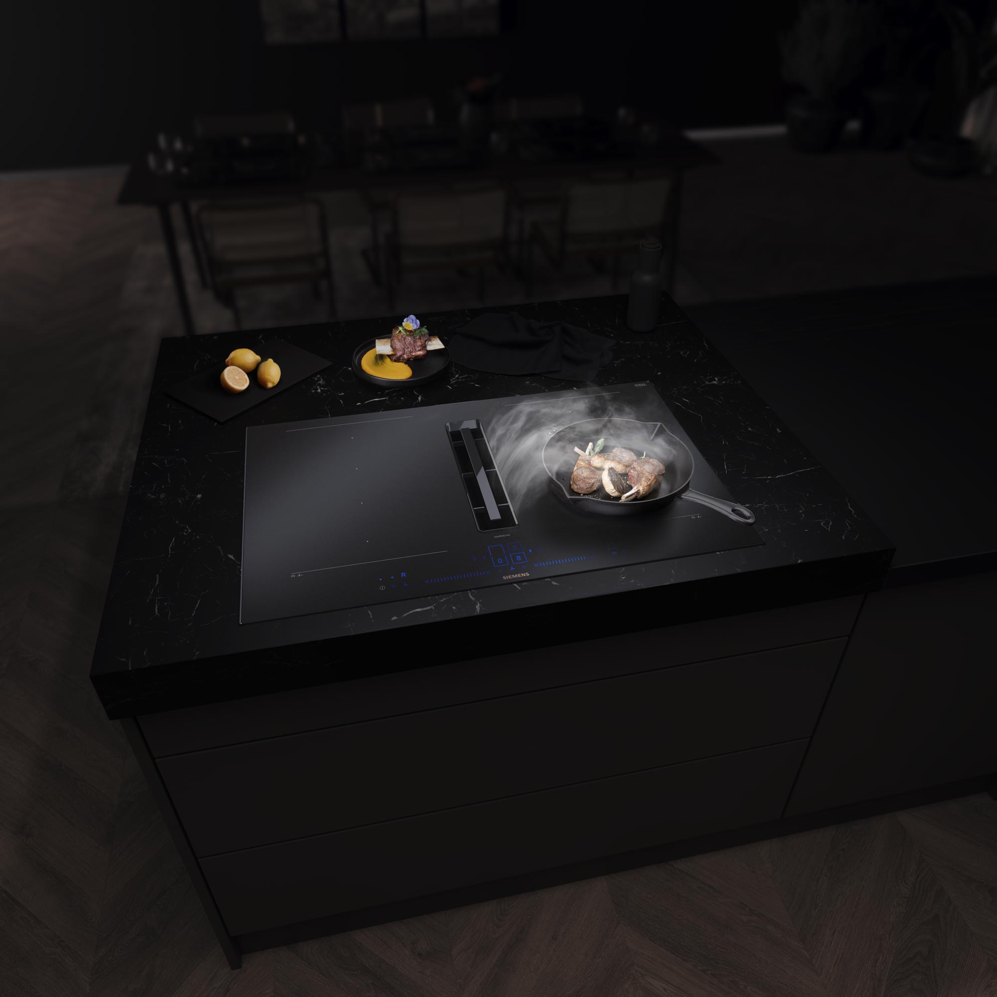 Eine moderne schwarze Kücheninsel mit einem Induktionskochfeld von Siemens und einer integrierten Dunstabzugshaube. In einer Pfanne dampft gerade etwas, und daneben liegt Brot mit Aufstrich auf einem Schneidebrett. Im Hintergrund ist ein Esstisch bei gedämpftem Licht zu sehen.